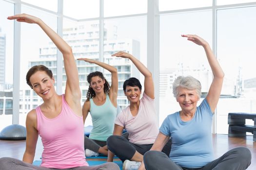 Happy female trainer with class stretching hands at yoga class