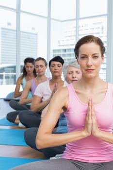Female trainer and class sitting with joined hands in a row at yoga class