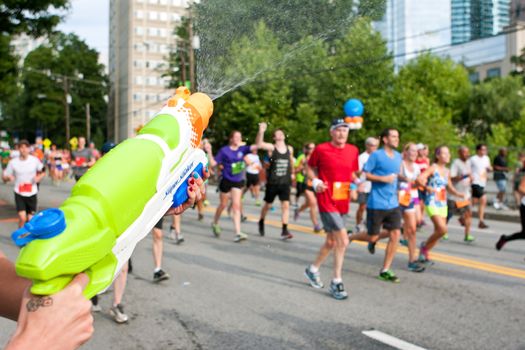 Atlanta, GA, USA - July 4, 2014:  A woman soaks runners with a squirt gun as they head toward the finish line of the Peachtree Road Race.