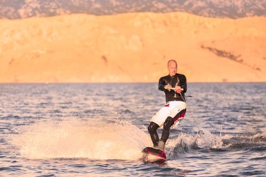 Wakeboarder in colorful shorts riding in sunset.