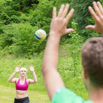 Young sporty couple playing volleyball outdoors in park. Healthy active lifestyle. Activities in nature.