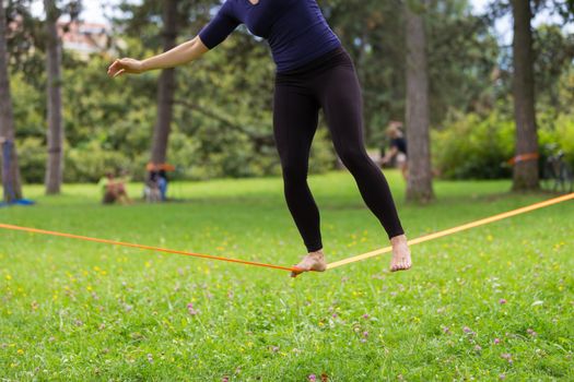 Lady practising slack line in the city park. Slacklining is a practice in balance that typically uses nylon or polyester webbing tensioned between two anchor points.