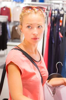 Woman shopping clothes. Shopper looking at clothing indoors in store. Beautiful blonde caucasian female model. 