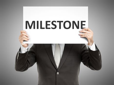 A business man holding a paper in front of his face with the text milestone