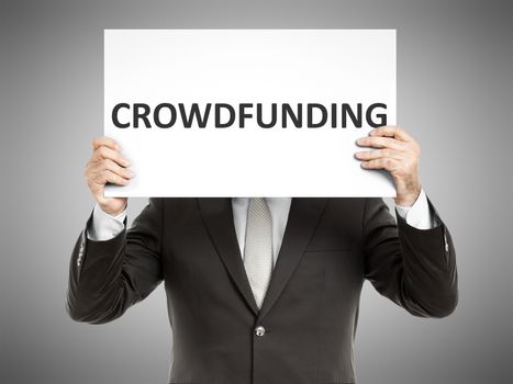 A business man holding a paper in front of his face with the text crowdfunding