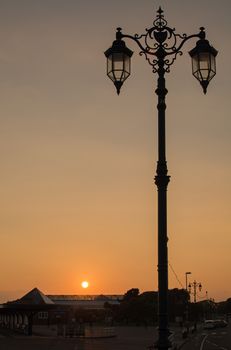 An ornate streetlamp, silhouetted against the setting sun