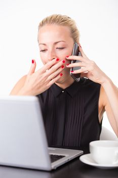 Work late into the night. Business woman yawning while talking on the mobile home and checking some information on her laptop computer in office. White cup of coffee on the desk. 