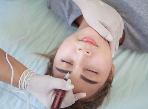 Professional permanent makeup applying on eyebrow