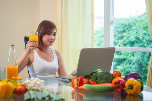 Young asian woman drinking orange juice and using internet at home