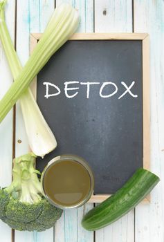 Detox handwritten on a blackboard with a green vegetable smoothie and ingredients