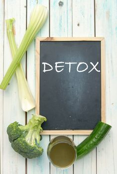 Detox handwritten on a blackboard with a green vegetable smoothie and ingredients