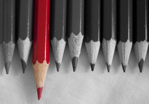 Red pencil amongst a row of pencils in black and white