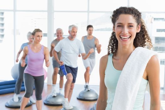 Portrait of a cheerful young woman with people exercising in the background at fitness studio