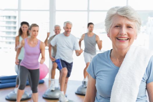 Portrait of a cheerful senior woman with people exercising in the background at fitness studio