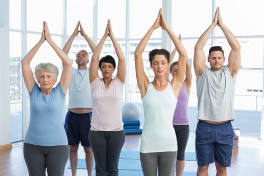 Sporty people with eyes closed and joined hands at a bright fitness studio