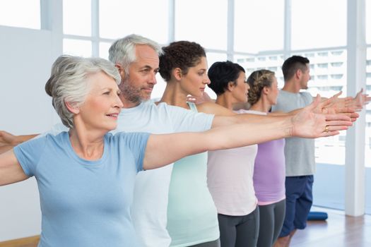 Portrait of fitness class stretching hands in row at yoga class