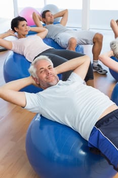 Portrait of smiling people stretching on exercise balls in the bright gym