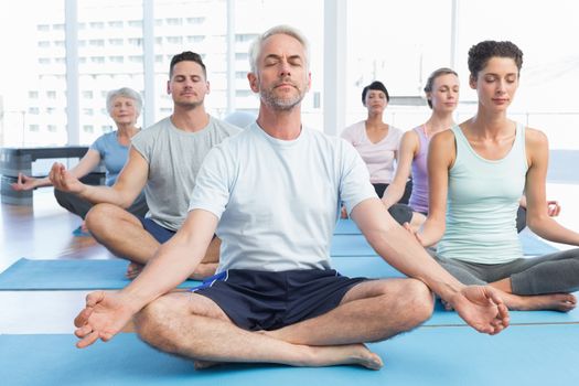 Sporty people in lotus pose with eyes closed at a bright fitness studio