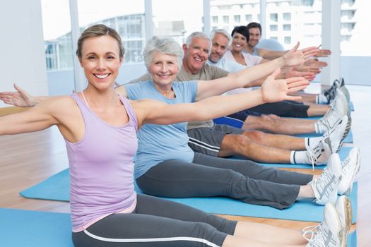 Happy female trainer with class stretching hands at yoga class