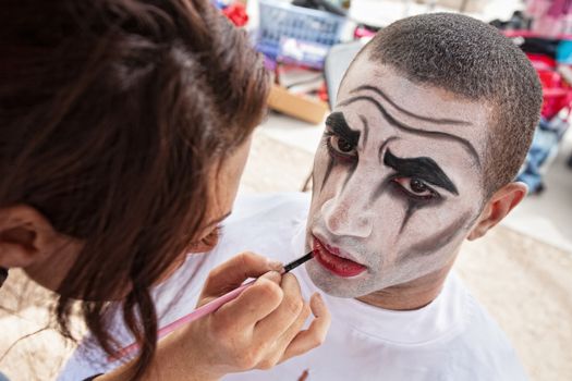 Makeup artist lining lips of male circus clown