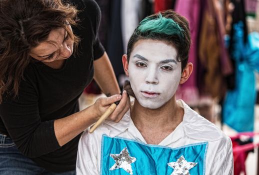 Makeup artist brushing white on serious young cirque performer