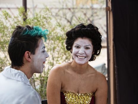 Two cirque performers in makeup laughing backstage