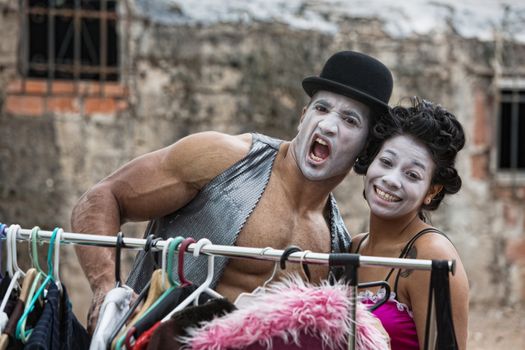 Laughing cirque clowns with makeup at clothing rack