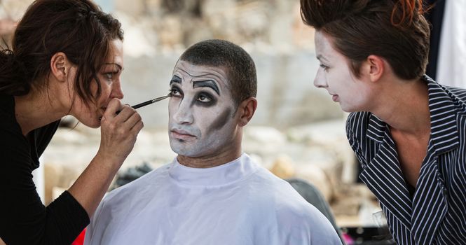 Handsome male clown with stylist putting on eye shadow