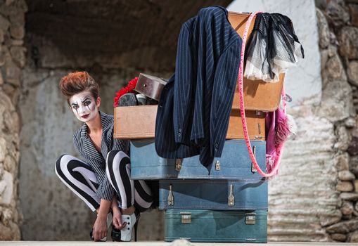 Grinning female clown squatting near stack of suitcases