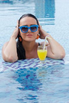 Woman drinking a fruit juice and enjoying in a swimming pool during a sunny day . Summer and holiday concept