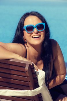 Woman in swimsuit with sunglasses  laying on chaise-longue poolside Done with a retro vintage  filter.