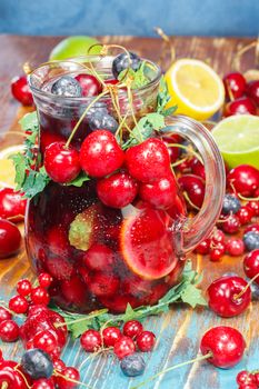 Refreshing fruit punch beverage in pitcher over rustic wooden background. Heart-shaped pair of cherries on top