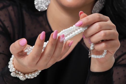 Beads pearls. Beautiful woman hands with pink manicure holding white pearl necklace.. Pearls and Nails concept
