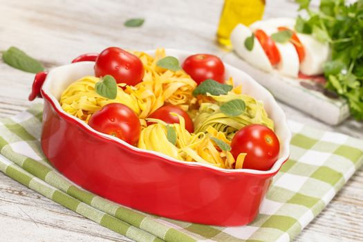 Italian pasta in heart shaped bowl with ingredients. Pasta with tomatoes, olive oil and mozzarella cheese. Ready to cook. Close up. Macro.