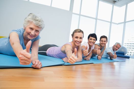Fitness group gesturing thumbs up in row at the yoga class