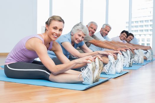 Happy female trainer with class stretching hands to legs at yoga class