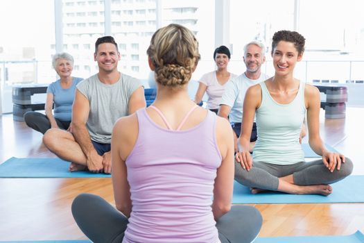 Trainer with sporty people sitting on exercise mats at a bright fitness studio