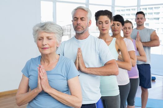 Sporty people with eyes closed and joined hands at a bright fitness studio