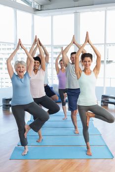 Portrait of a smiling trainer with class standing in tree pose at yoga class