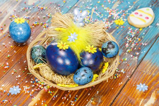 Boiled Easter eggs in basket on wooden rustic table with tulip and colorful crumbs. Macro, selective focus