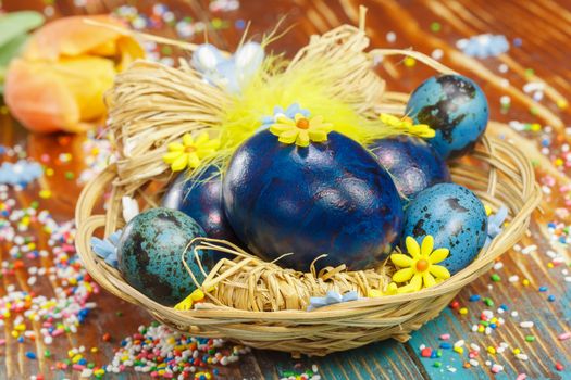 Boiled Easter eggs in basket on wooden rustic table with tulip and colorful crumbs. Macro, selective focus