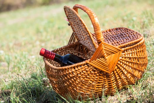 Picnic basket with bottle of red dry wine placed on grass