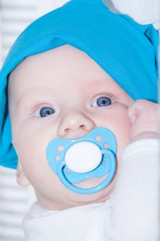Caucasian 3 month old baby boy with big blue eyes and long eyelashes has a blue blanket and pacifer in his mouth