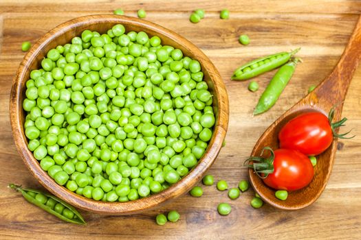 Fresh green peas and tomato on wooden background