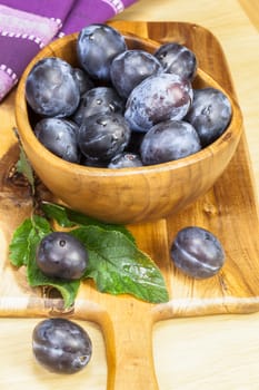 Fresh plums with leaves in bowl on wooden table