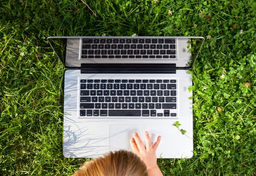 Tpo view of little girl usng laptop in a summer garden
