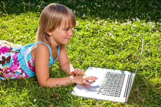 Little girl usng laptop in a summer garden