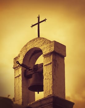 Photo of a old Mediterranean Church Top with bell and a cross, artistic toned photo