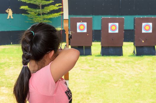 Young girl holding and aiming bow in practice field
