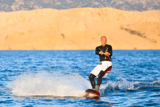 Wakeboarder in wetsuit riding in sunset. Wakeboarding is a surface water sport which involves riding a wakeboard over the surface of a body of water.